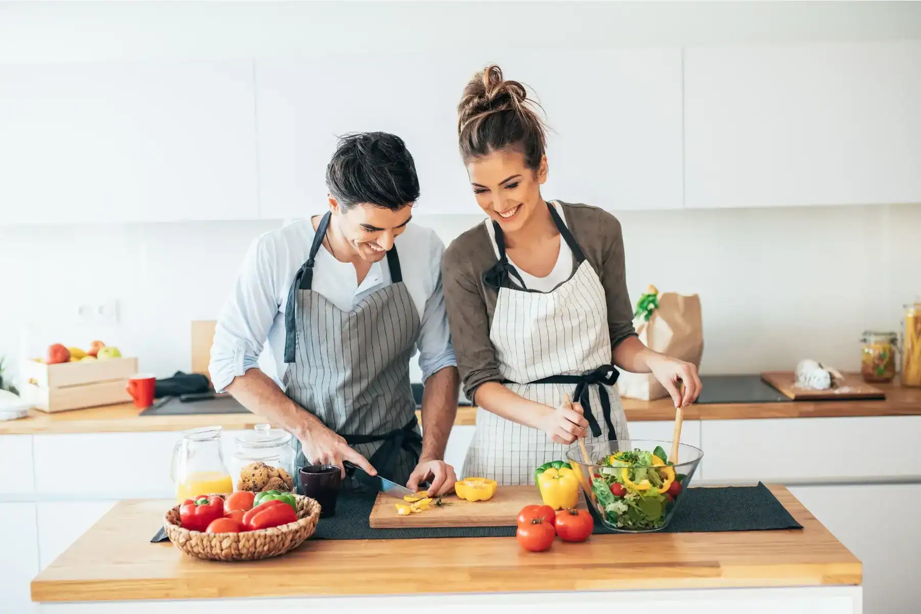 Couples Nutrition Counselling, A smiling man and woman wearing aprons prepare food together in a bright kitchen. 